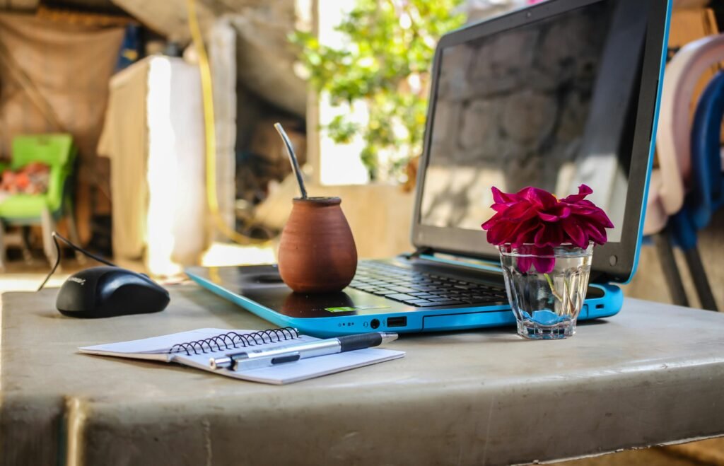 A serene outdoor workspace featuring a laptop, notebook, mug, and flowers on a desk.