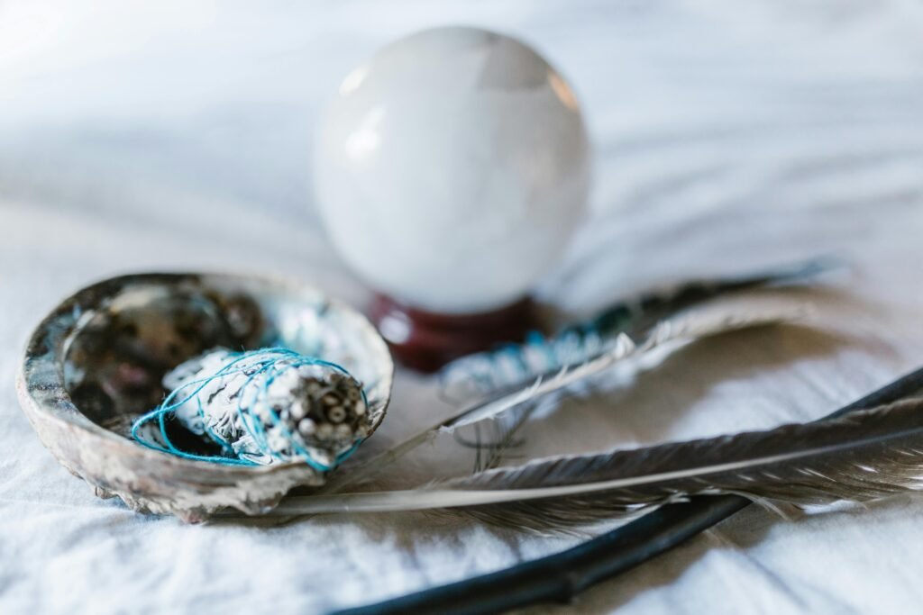 A spiritual arrangement featuring a crystal ball, sage bundle, and feathers, ideal for mystical themes.